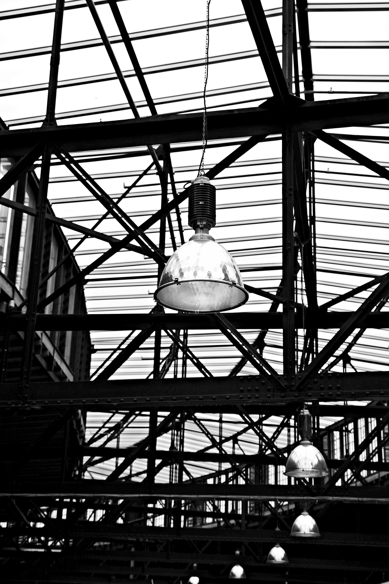 Schwarz-Weiß-Foto von industriellen Deckenlampen, die von einer Metallkonstruktion in einer Halle hängen. So kann man in der Industrie Energie sparen.