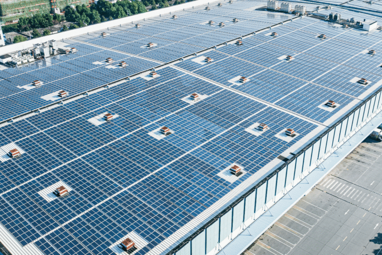 Luftaufnahme eines Fabrikdachs mit Solar Panelen. Im Hintergrund sieht man die Skyline einer Stand mit Hochhäusern.