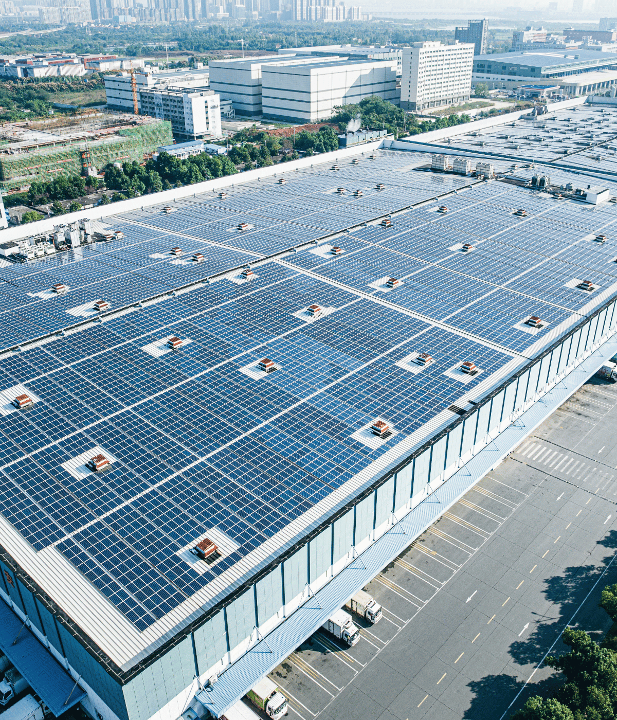 Luftaufnahme eines Fabrikdachs mit Solar Panelen. Im Hintergrund sieht man die Skyline einer Stand mit Hochhäusern.